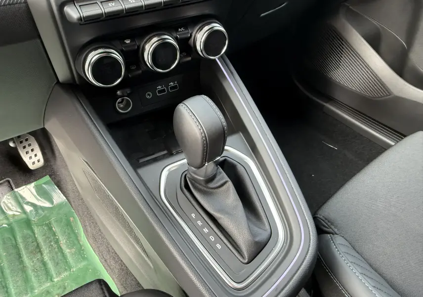 Gros plan sur la console centrale de la Renault Clio V hybride 2025, avec levier de boîte auto et commandes de climatisation.