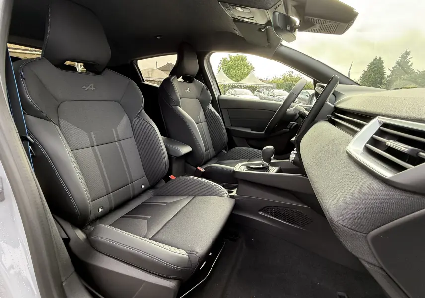 Intérieur avant de la Renault Clio V 1.6 E-TECH gris Rafale, sièges sport Alpine noirs avec surpiqûres bleues visibles côté gauche.
