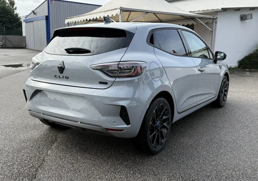 Renault Clio V gris Rafale vue 3/4 arrière droit, avec jantes noires et vitres teintées sur parking extérieur.