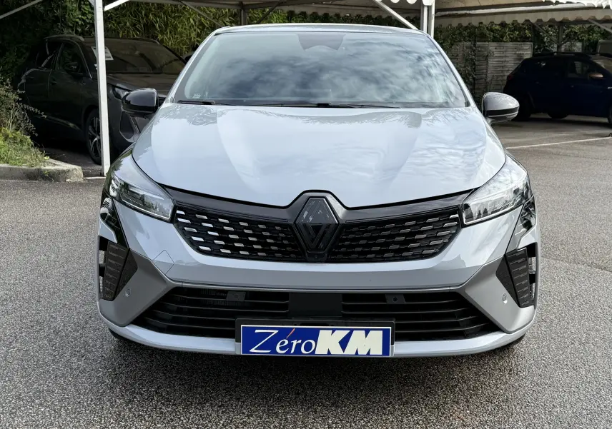 Vue frontale d'une Renault Clio V gris rafale avec calandre noire et plaque d'immatriculation "Zéro KM" visible.