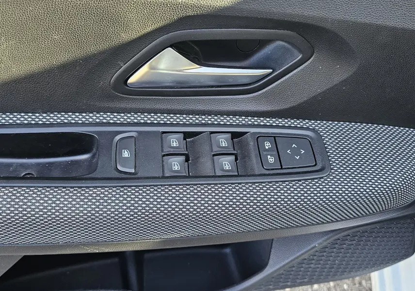 Gros plan sur la commande des vitres électriques et la poignée intérieure côté conducteur d’une Dacia Sandero III blanc glacier.