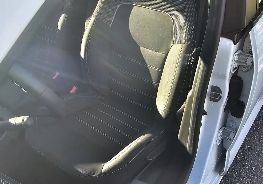 Vue intérieure côté conducteur de la Dacia Sandero III blanche, mettant en valeur le siège en tissu noir et la boîte manuelle.