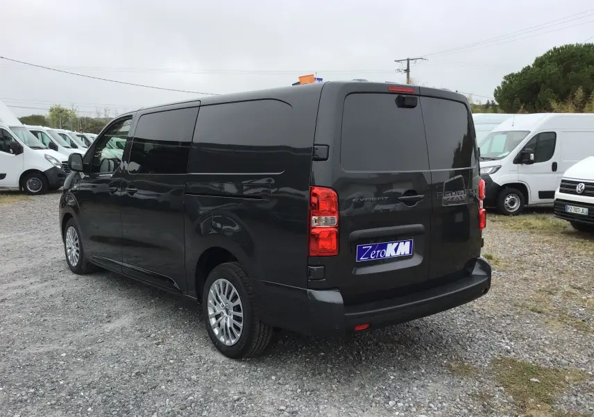 Vue 3/4 arrière droite d’un Peugeot Expert cabine approfondie gris titane, avec vitres arrière teintées et feux rouges visibles.