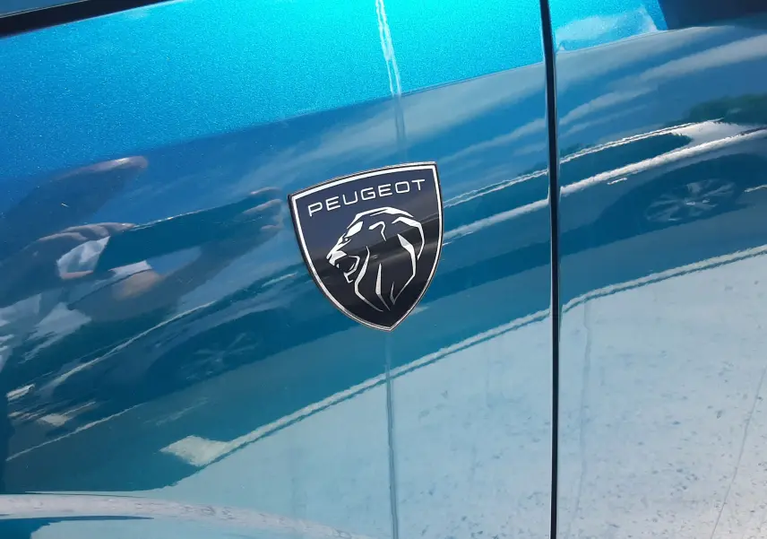 Gros plan sur l'écusson Peugeot sur la portière côté gauche d'un 3008 bleu obsession 2026.