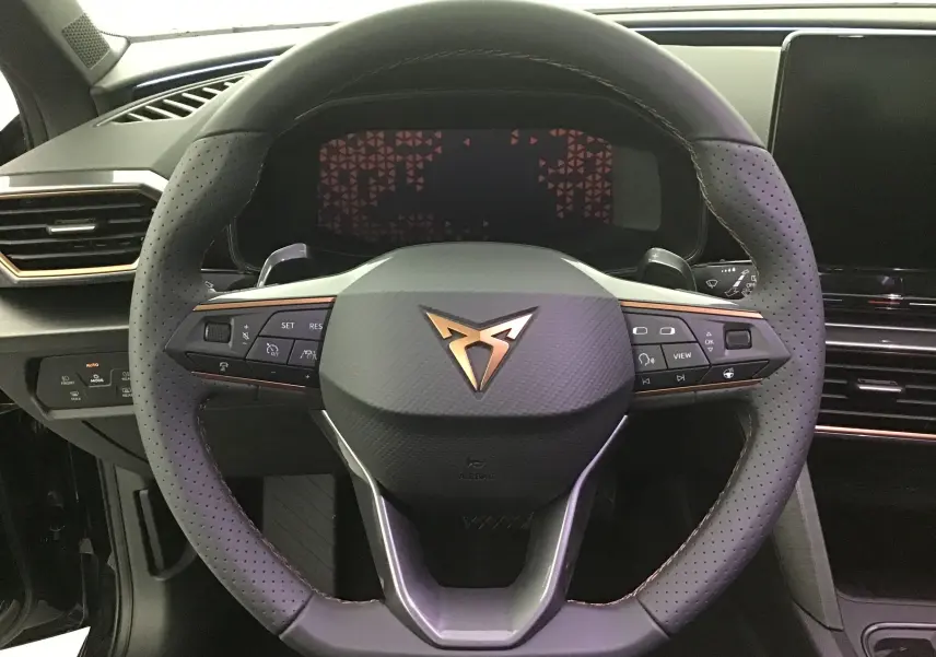 Vue rapprochée du volant noir perforé avec logo Cupra cuivré et commandes intégrées du tableau de bord d'une Leon 2023.