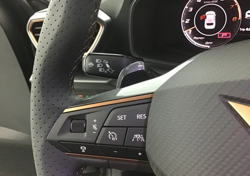 Gros plan sur le volant perforé noir de la CUPRA Leon 2023 avec commandes multifonctions et logo cuivre.