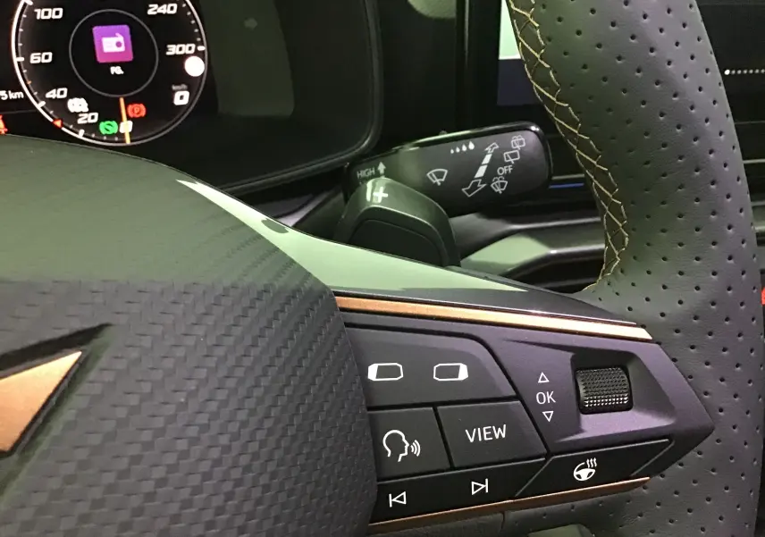 Gros plan sur le volant noir perforé avec surpiqûres cuivrées et commandes multifonctions du tableau de bord digital d'une CUPRA Leon 2023.
