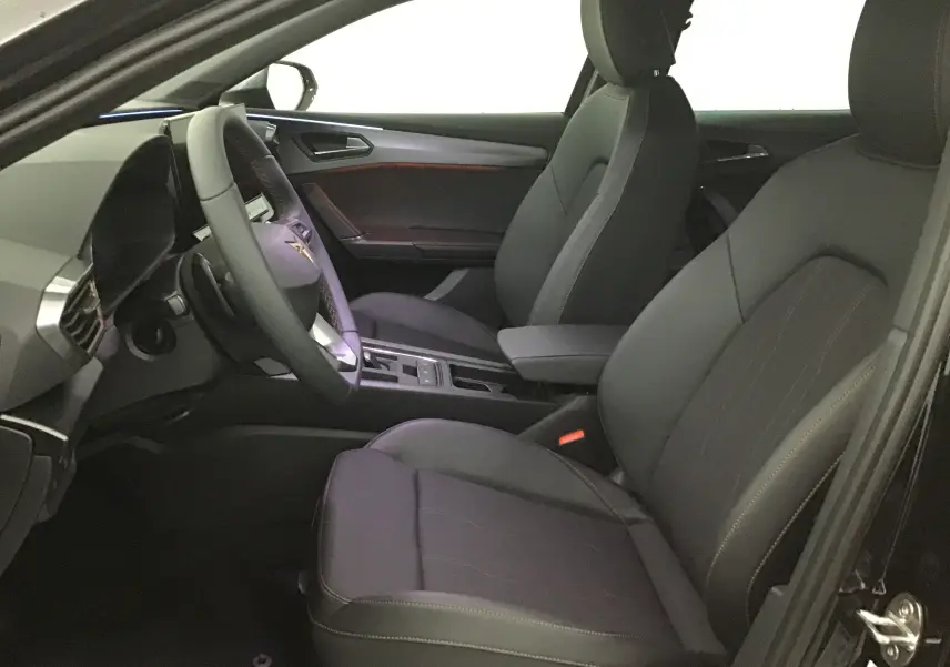 Vue intérieure côté conducteur de la CUPRA Leon noire 2023, sièges en cuir noir et tableau de bord moderne avec volant multifonction.
