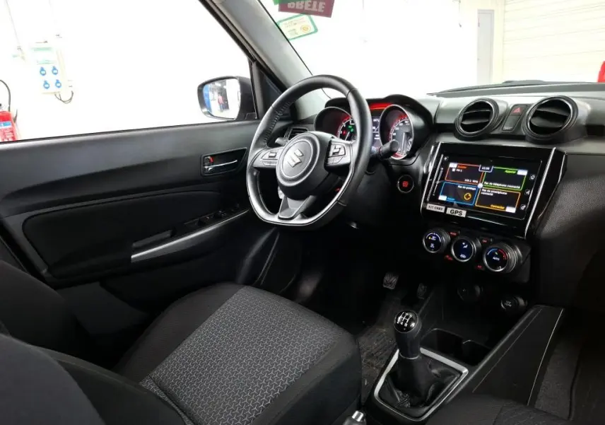 Vue intérieure côté conducteur de la Suzuki Swift grise 2023, avec volant multifonction, écran tactile et boîte manuelle.