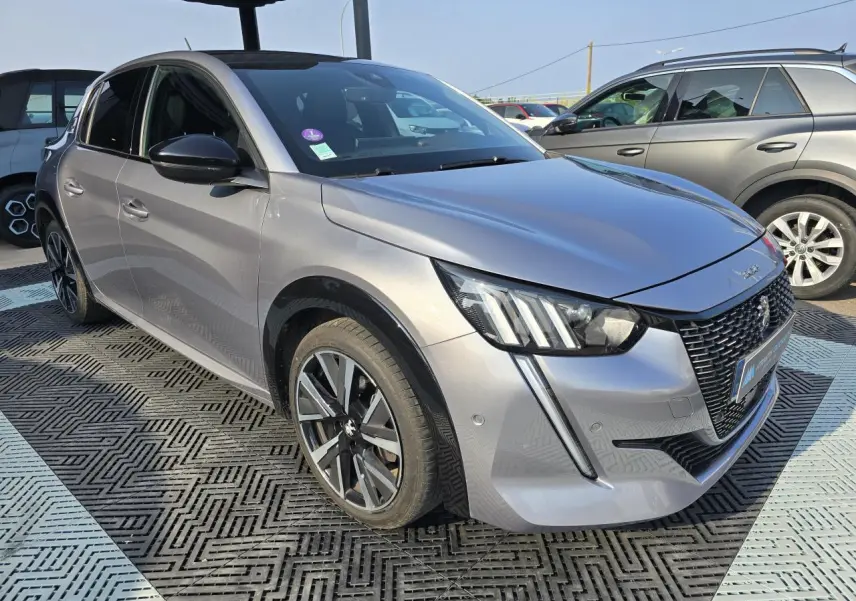 Peugeot 208 grise vue 3/4 avant droit, avec jantes alliage et toit noir sous un abri.