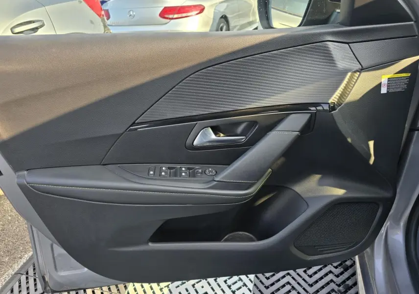 Vue intérieure côté gauche de la porte avant grise du Peugeot 208 II 1.2 GT PACK avec habillage carbone et commandes électriques.