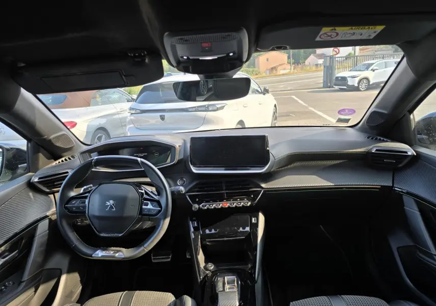 Vue intérieure avant du Peugeot 208 gris 2023, mettant en valeur le volant compact, l'écran tactile central et la planche de bord noire.
