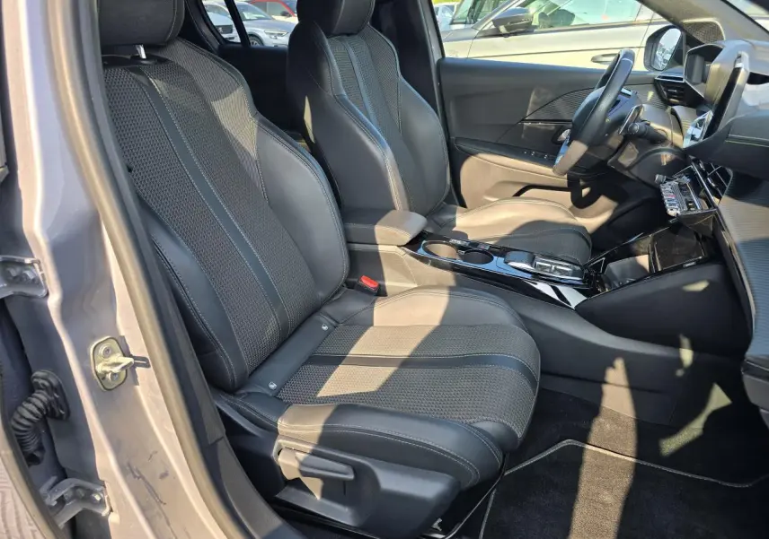 Vue intérieure côté gauche avant de la Peugeot 208 grise 2023, sièges sport en tissu et cuir avec console centrale brillante noire.