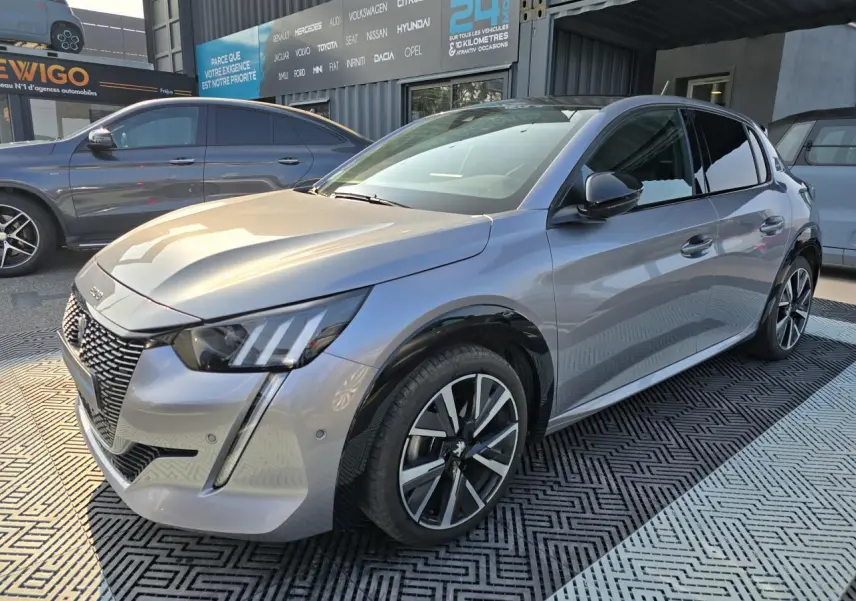 Peugeot 208 grise vue 3/4 avant droit avec jantes alliage et toit noir brillant dans un showroom extérieur.