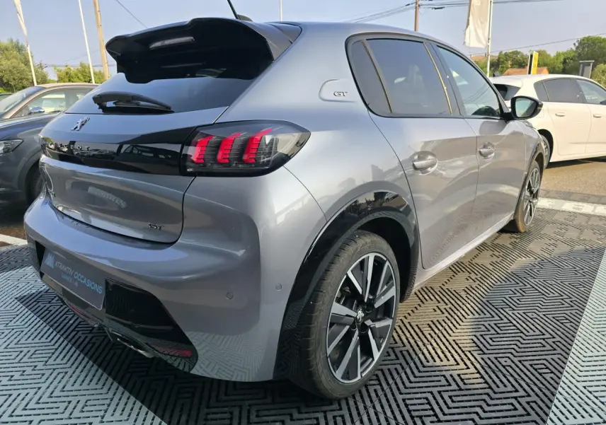 Vue 3/4 arrière droite d'une Peugeot 208 grise 2023 avec toit noir, feux arrière LED et jantes alliage 17 pouces.