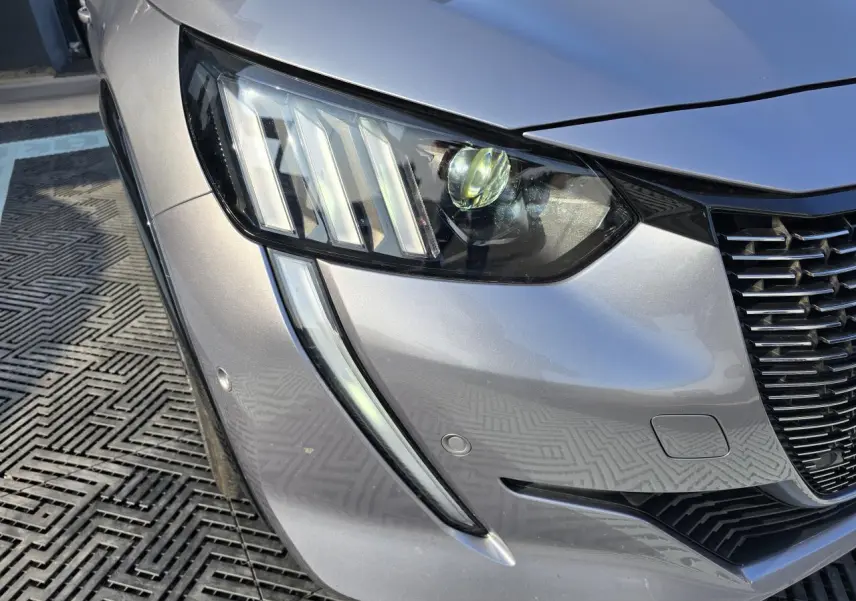 Gros plan sur le phare avant droit gris métallisé de la Peugeot 208 avec sa signature lumineuse verticale distinctive.