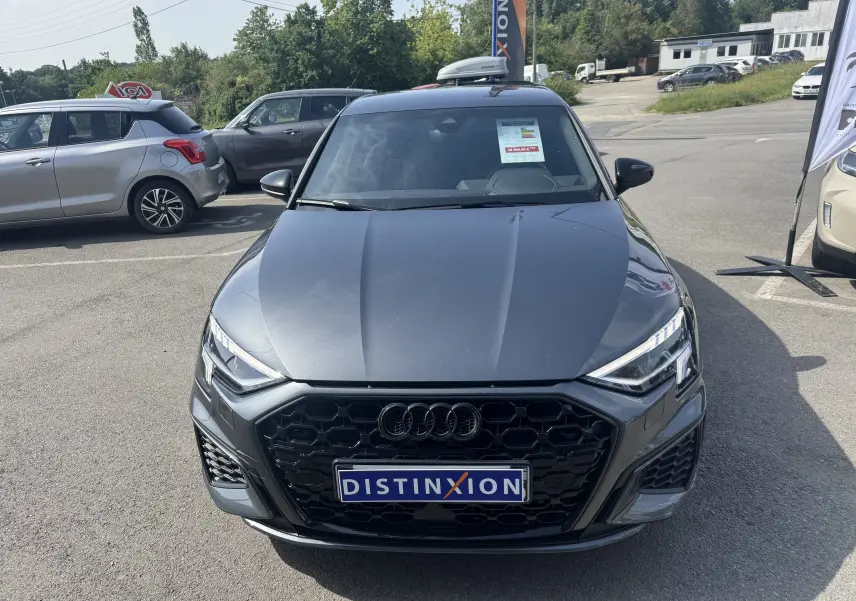 Vue avant d'une Audi A3 Sportback TDI 2.0 S-Line gris, avec calandre noire et plaque Distinxion visible.