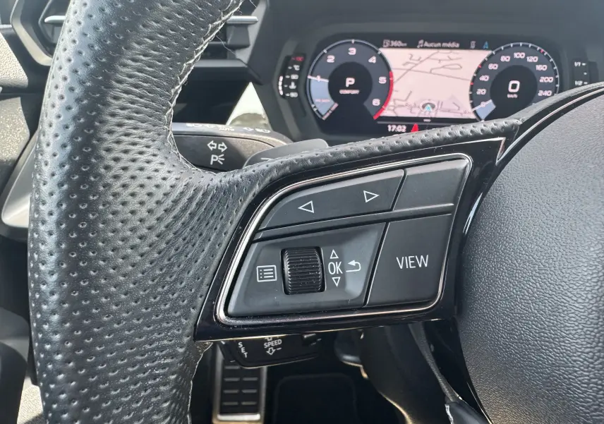Gros plan sur les commandes à droite du volant perforé noir de l'Audi A3 Sportback TDI 2.0 S-Line 2023 avec tableau de bord numérique.