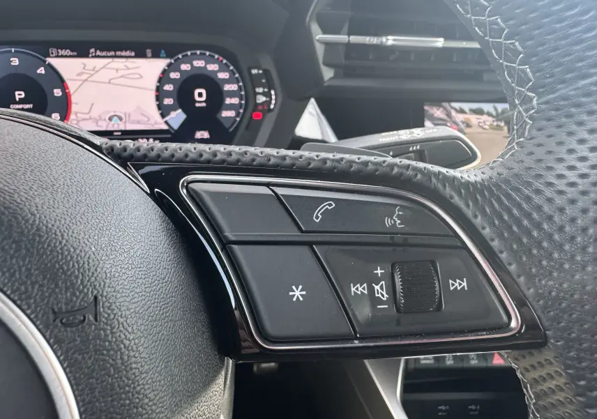 Gros plan sur les commandes au volant à droite de l'Audi A3 Sportback gris 2023, avec tableau de bord numérique en arrière-plan.