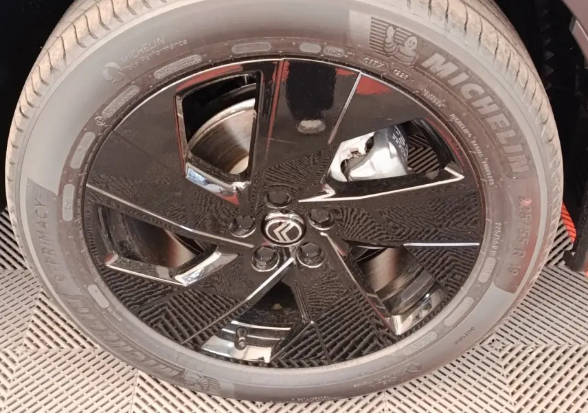 Gros plan sur la jante noire brillante avec logo Citroën et pneu Michelin du Citroën C5 Hybride vert.