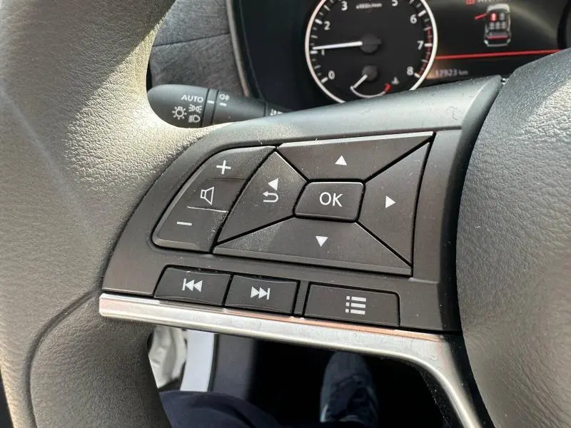 Gros plan sur les commandes multifonctions au volant côté gauche du Nissan Juke blanc nacré 2025, avec tableau de bord en arrière-plan.