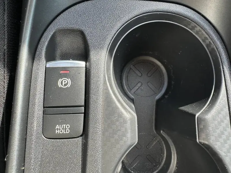 Gros plan sur la commande de frein à main électronique et porte-gobelets noirs dans l'habitacle du Nissan Juke blanc nacré 2025.