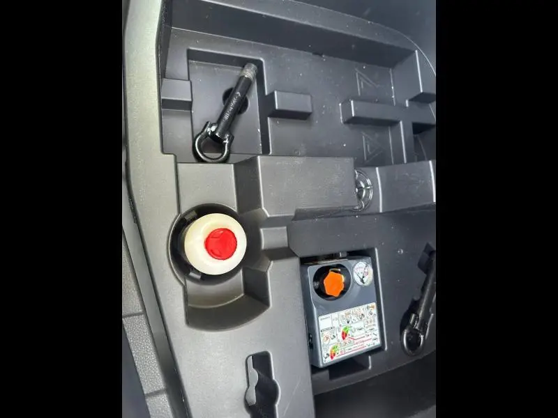 Détail du coffre avec kit de réparation pneu et outils noirs sur fond plastique gris du Nissan Juke blanc nacré 2025.
