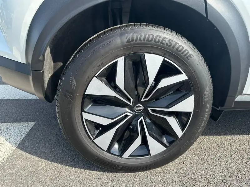 Gros plan sur la roue avant gauche du Nissan Juke blanc nacré avec jante alliage noire et argentée au design moderne.