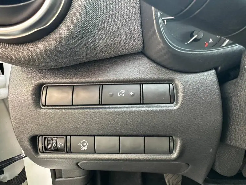 Détail des commandes d’éclairage et réglage de luminosité sur le tableau de bord côté gauche du Nissan Juke blanc nacré 2025.