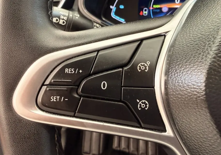 Gros plan sur les commandes du régulateur de vitesse au volant cuir synthétique d'une Renault Clio blanche hybride 2022.