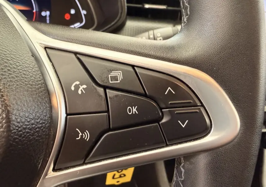 Gros plan sur les commandes multifonctions noires du volant cuir synthétique de la Renault Clio Business E-Tech hybride 2022.
