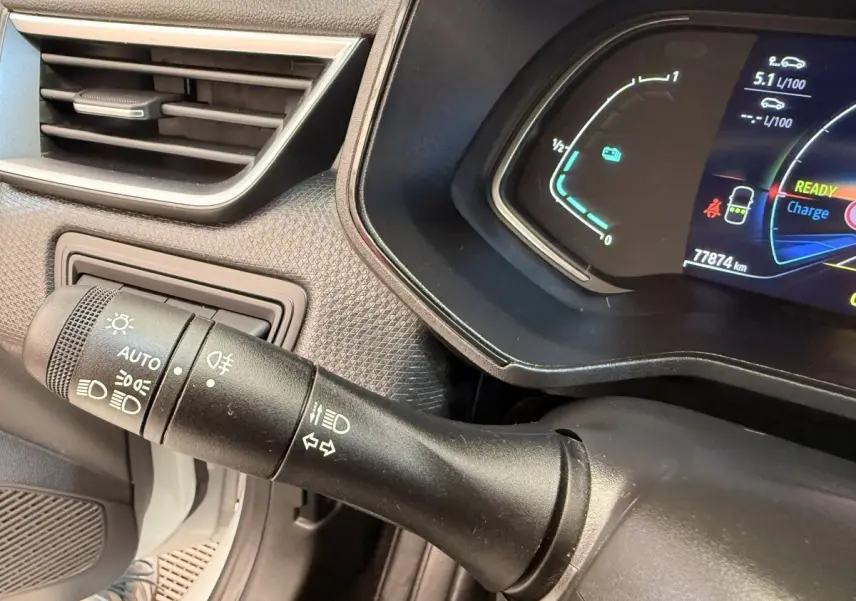 Gros plan sur la commande des phares et clignotants à gauche du tableau de bord numérique d’une Renault Clio blanche hybride.