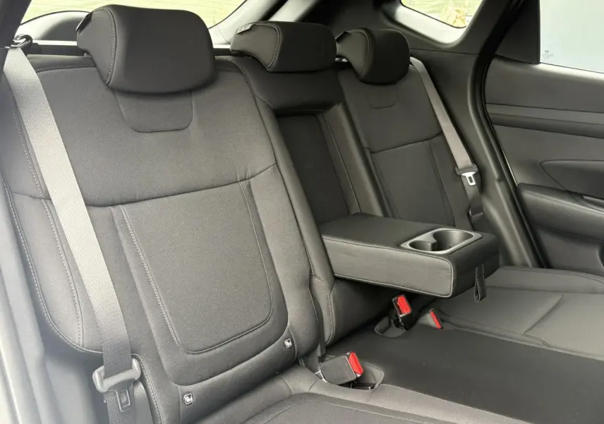 Vue intérieure des sièges arrière noirs du Hyundai Tucson 2026 avec accoudoir central et ceintures visibles côté droit.
