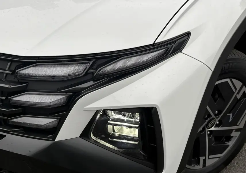 Gros plan sur l'avant droit blanc Atlas du Hyundai Tucson 2026, mettant en valeur les phares bi-LED et la jante alliage.