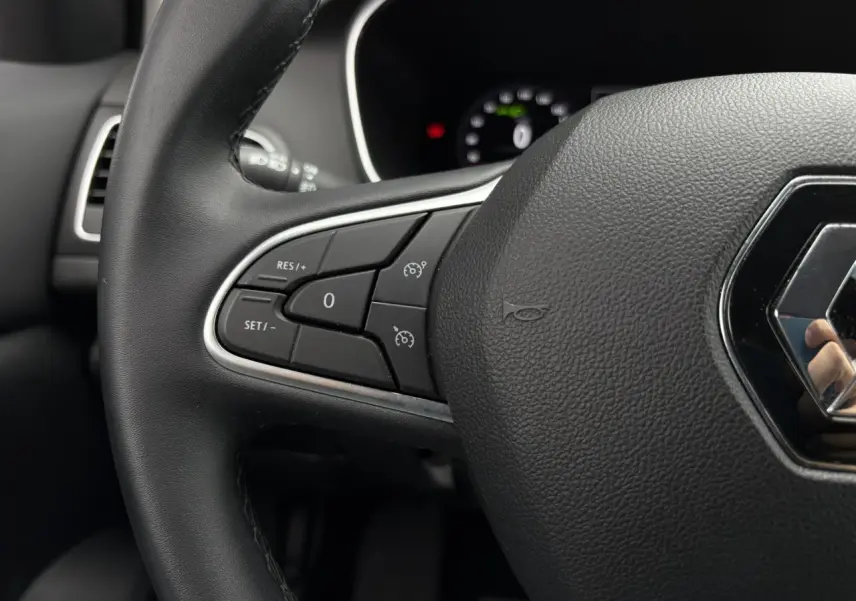 Gros plan sur le volant noir de la Renault Megane Break 2024 avec commandes de régulateur de vitesse à gauche.