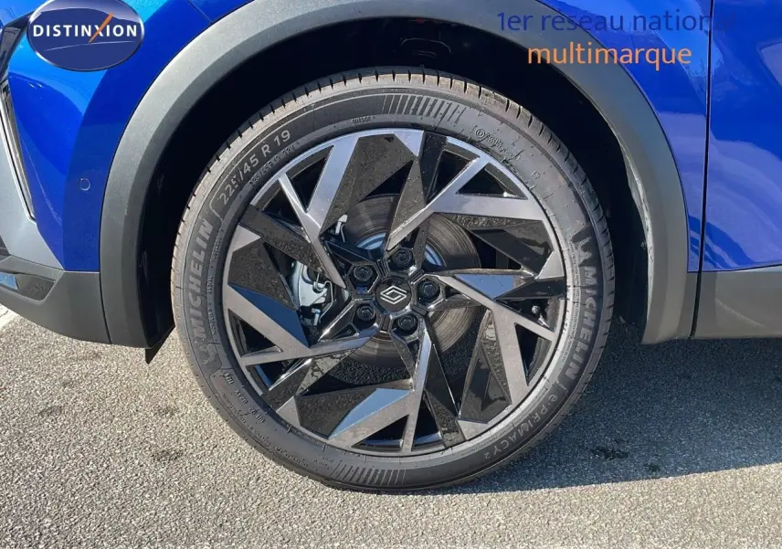 Gros plan sur la roue avant gauche du Renault Captur bleu Iron Metal avec jante alliage noire au design géométrique.