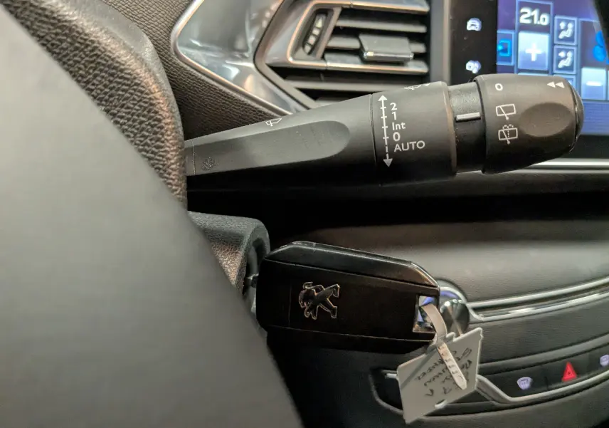 Gros plan sur la clé noire Peugeot insérée près du commodo d’essuie-glace, avec partie du tableau de bord et écran tactile visible.