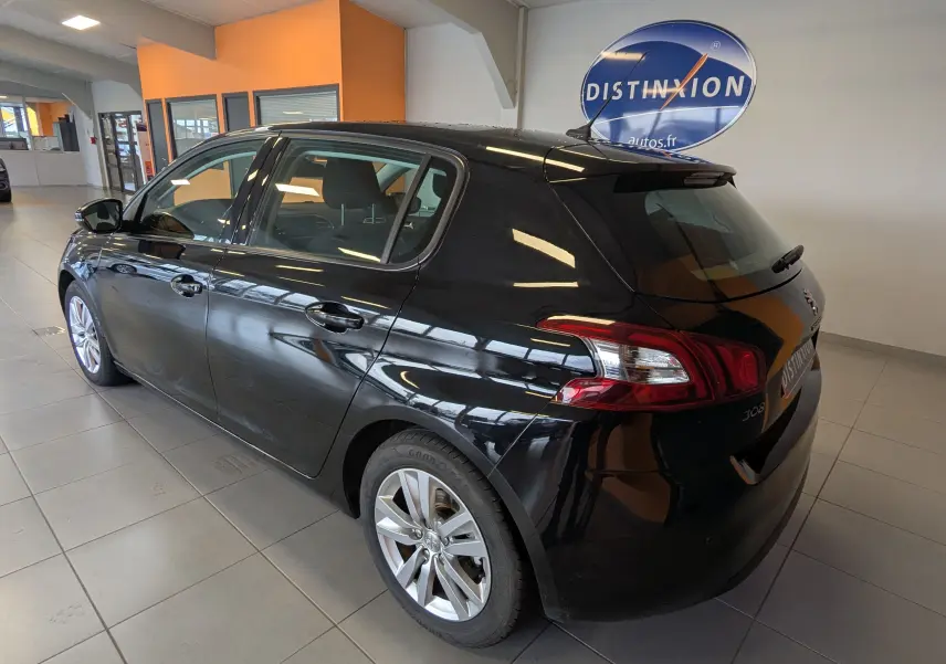 Vue 3/4 arrière côté gauche d'une Peugeot 308 noire 5 portes dans un showroom avec logo Distinxion en arrière-plan.