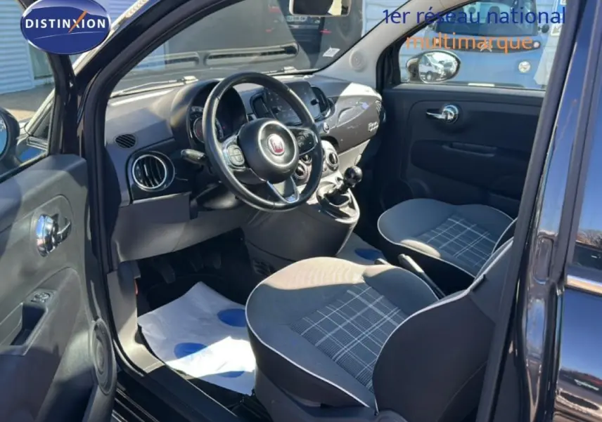 Vue intérieure côté conducteur de la Fiat 500 noire, montrant le volant, la boîte manuelle et les sièges à motifs gris.