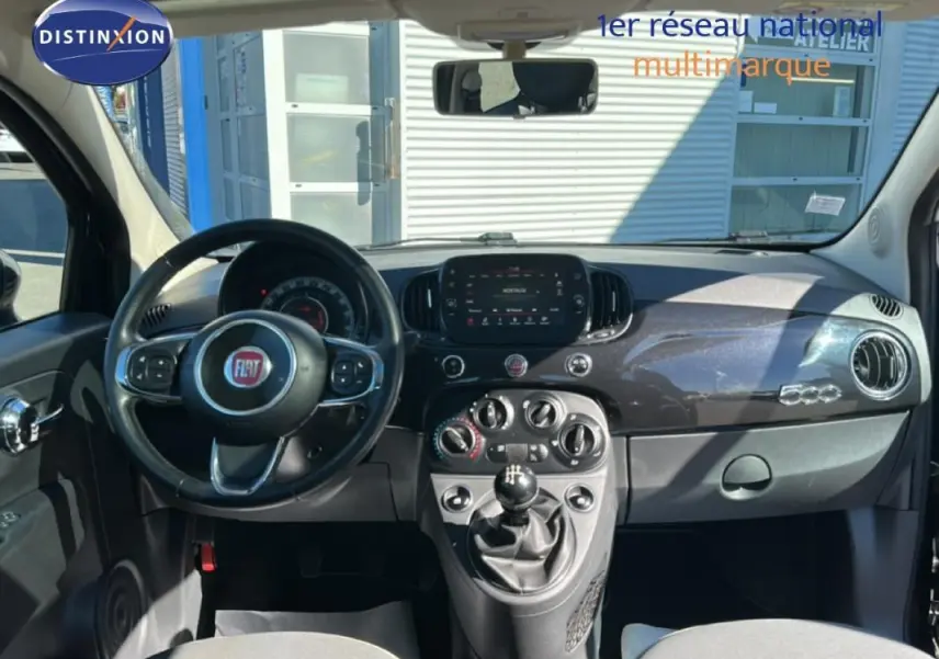 Vue intérieure frontale du tableau de bord noir brillant de la Fiat 500 Lounge 2016 avec volant multifonction et levier de vitesse manuel.