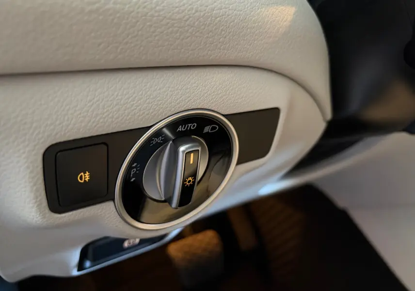 Gros plan sur le bouton de commande des phares avec éclairage allumé, intérieur cuir gris clair d'une Mercedes GLA 200D.