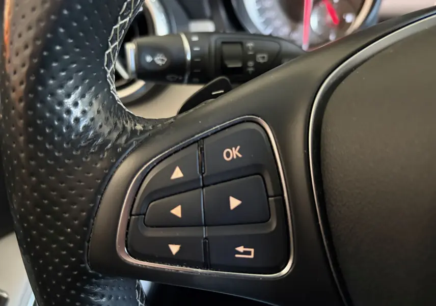 Gros plan sur les commandes multifonctions noires du volant cuir perforé d’une Mercedes GLA 200D Business gris de 2015.