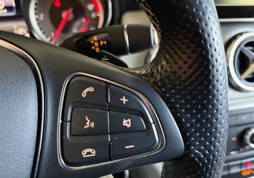 Gros plan sur les commandes multifonctions du volant en cuir perforé d’une Mercedes GLA 200D Business gris, intérieur gris.
