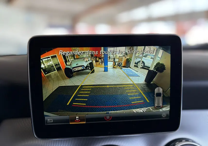 Écran multimédia du Mercedes GLA 200D Business affichant la caméra de recul avec vue intérieure sur tapis et véhicule ancien gris.