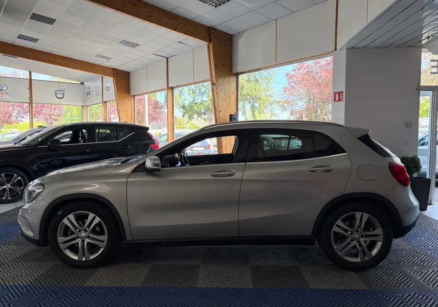 Vue de profil côté gauche d’un Mercedes GLA 200D Business gris exposé en showroom avec jantes alliage et intérieur visible.
