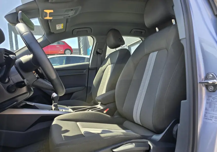 Vue intérieure côté conducteur de l'Audi A3 Sportback 2022, sièges gris avec bandes claires et volant cuir multifonctions.