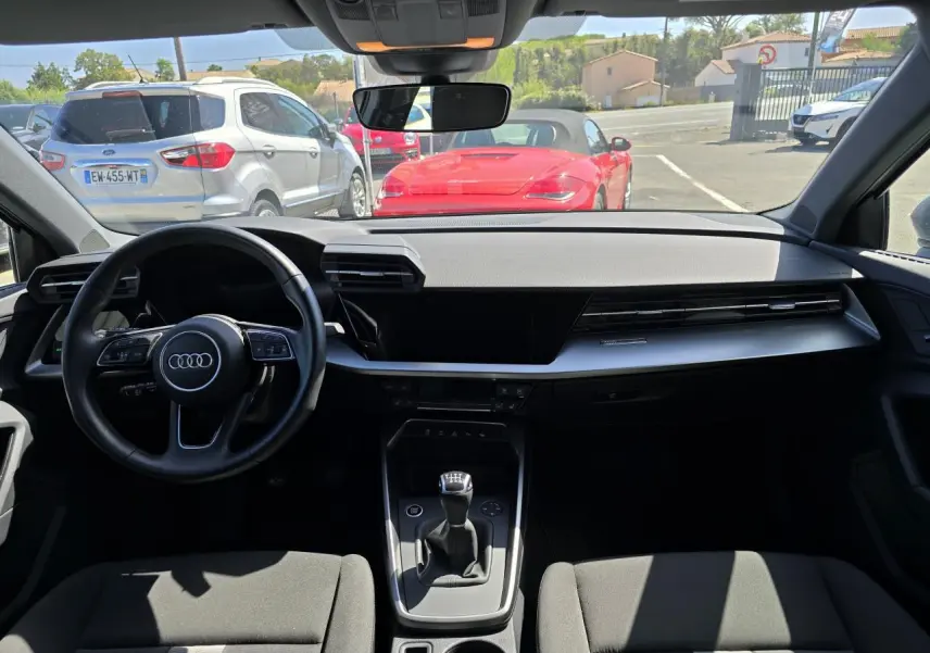 Vue intérieure avant de l'Audi A3 Sportback 2022 gris argent, volant cuir 3 branches et boîte manuelle visible.