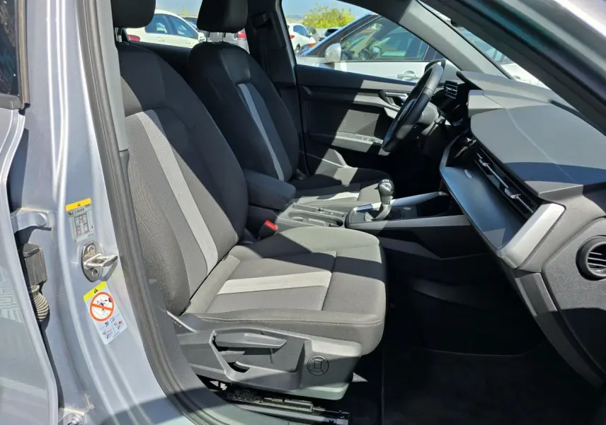 Vue intérieure côté conducteur de l'Audi A3 Sportback 2022 gris argent, avec sièges tissu bicolore et tableau de bord moderne.