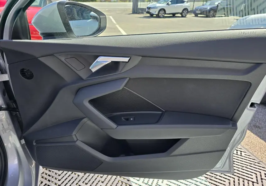 Vue de la porte avant gauche ouverte d’un Audi A3 Sportback gris argent, mettant en valeur la poignée et les haut-parleurs intégrés.