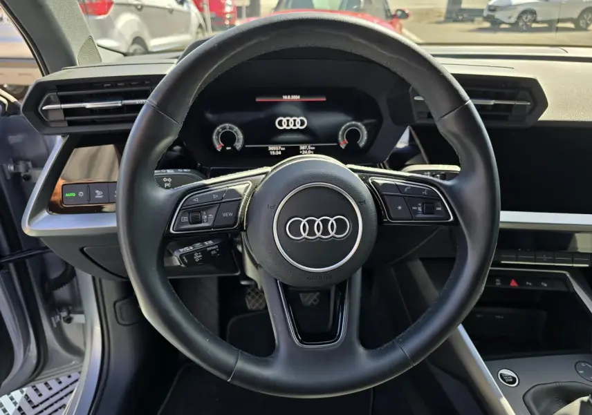 Vue intérieure centrée sur le volant cuir noir et l'Audi virtual cockpit d'une Audi A3 Sportback gris argent.
